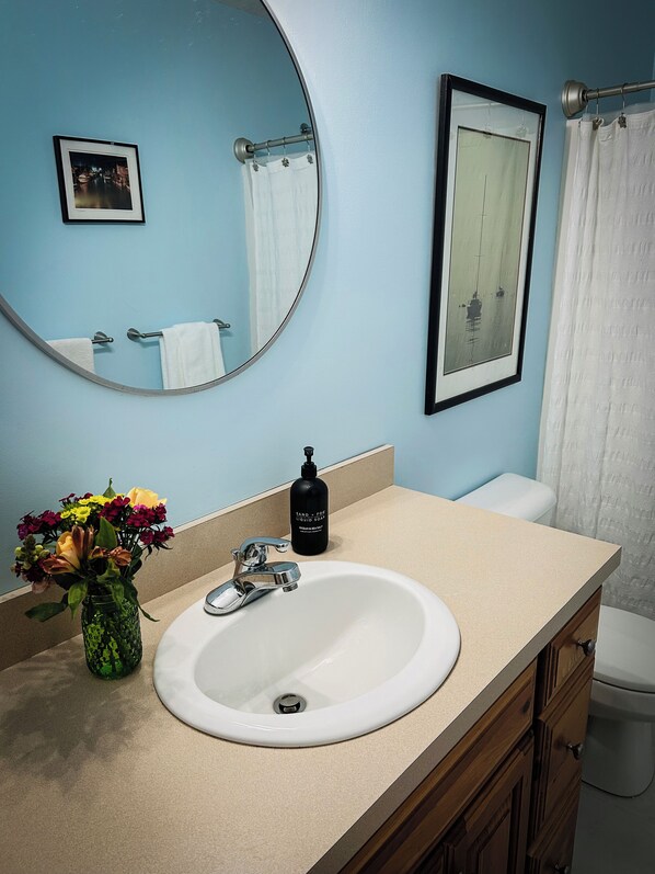 A bathroom with a round mirror, a sink, a toilet, and a shower curtain.