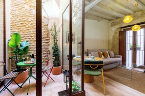 Un salon chaleureux avec un mur en pierre, une plante verte, une table en bois sur laquelle se trouve une bouteille de vin, et un canapé agrémenté de coussins.