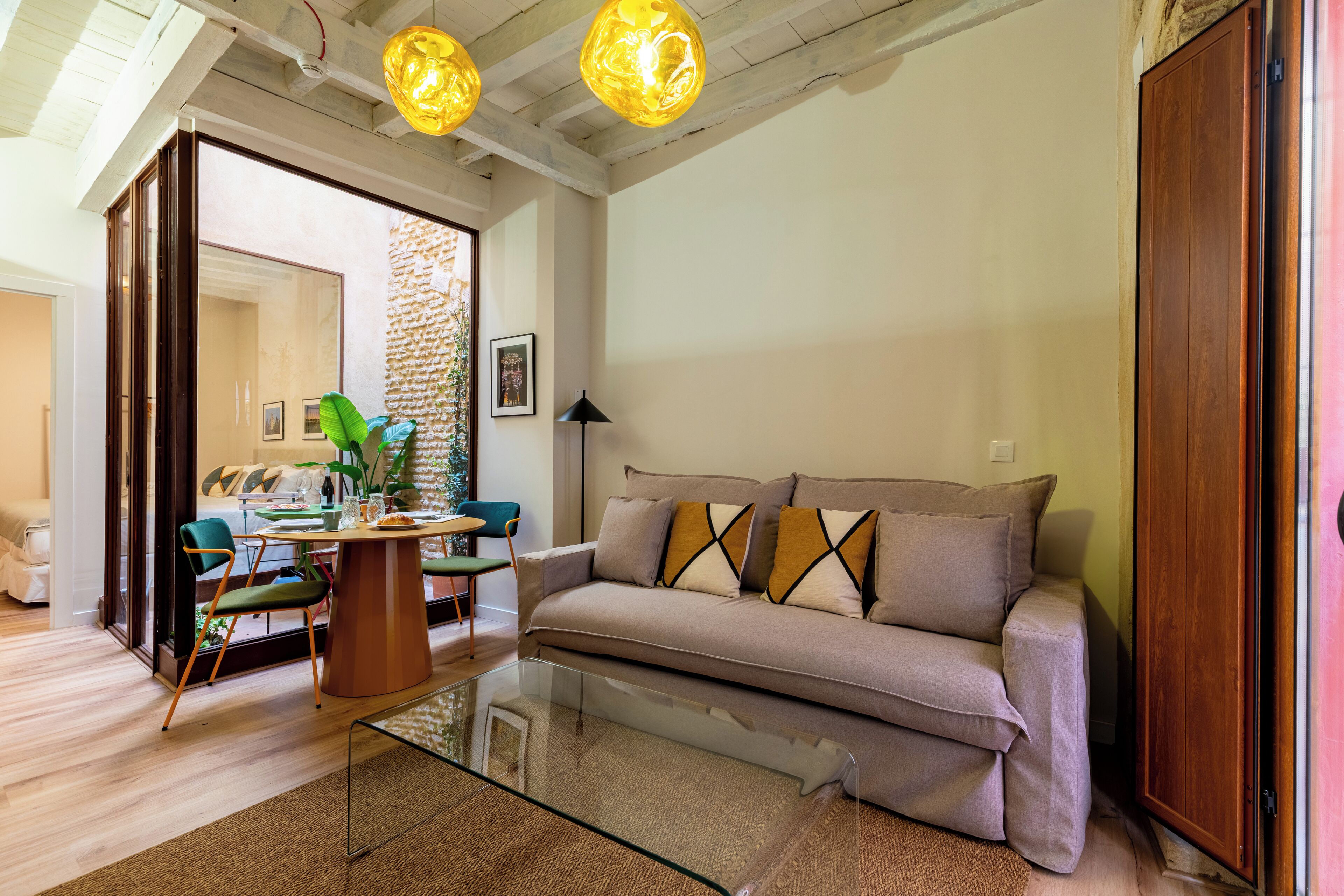 A modern living room with a sofa, glass coffee table, and a dining area with chairs and a table.