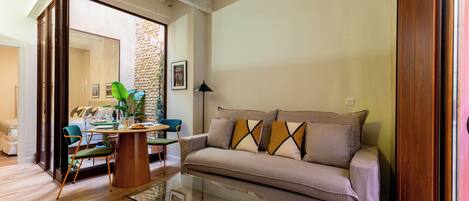 A modern living room with a sofa, glass coffee table, and a dining area with chairs and a table.