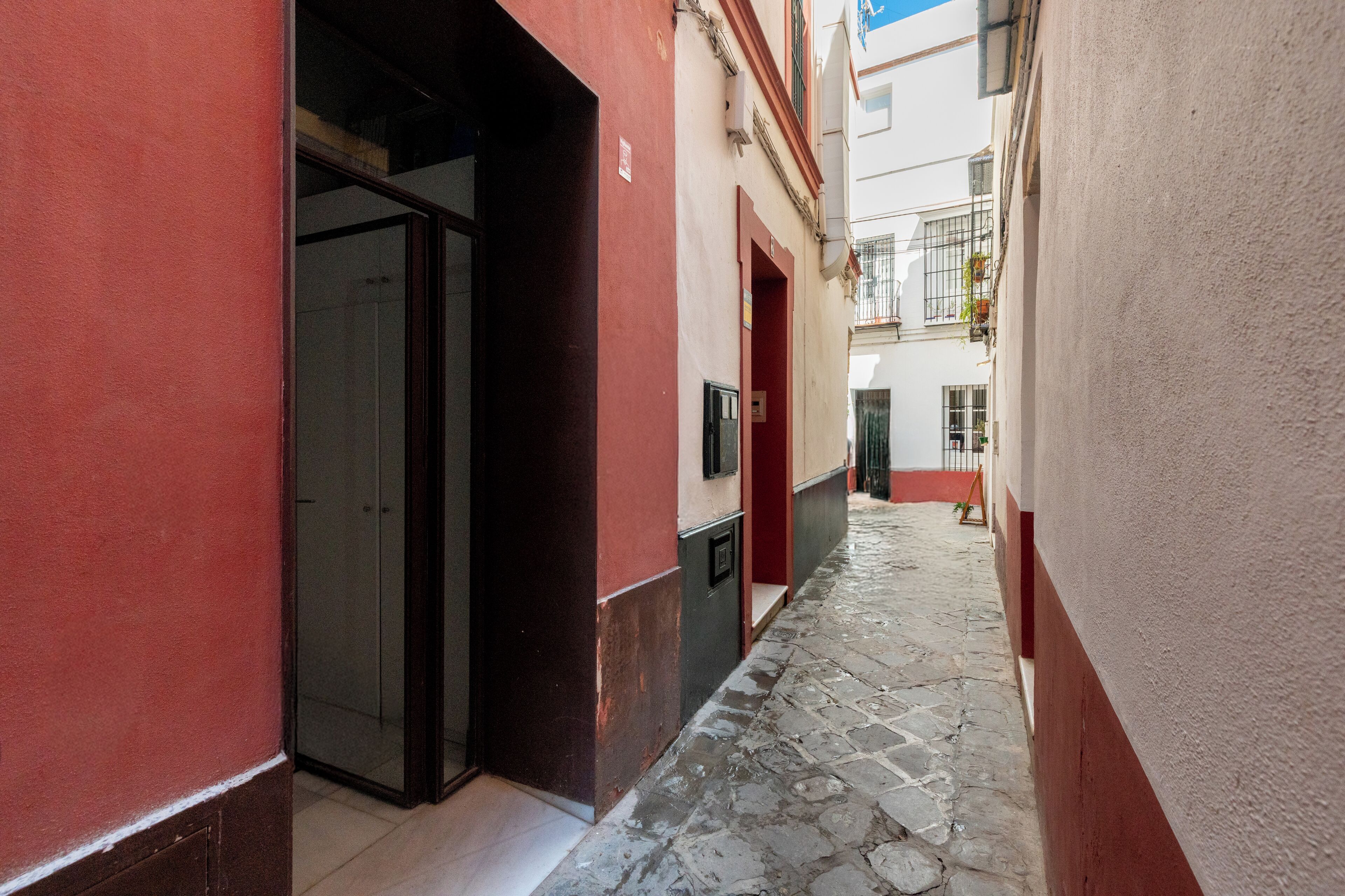 A narrow alleyway with a stone floor, flanked by buildings with red and white facades.