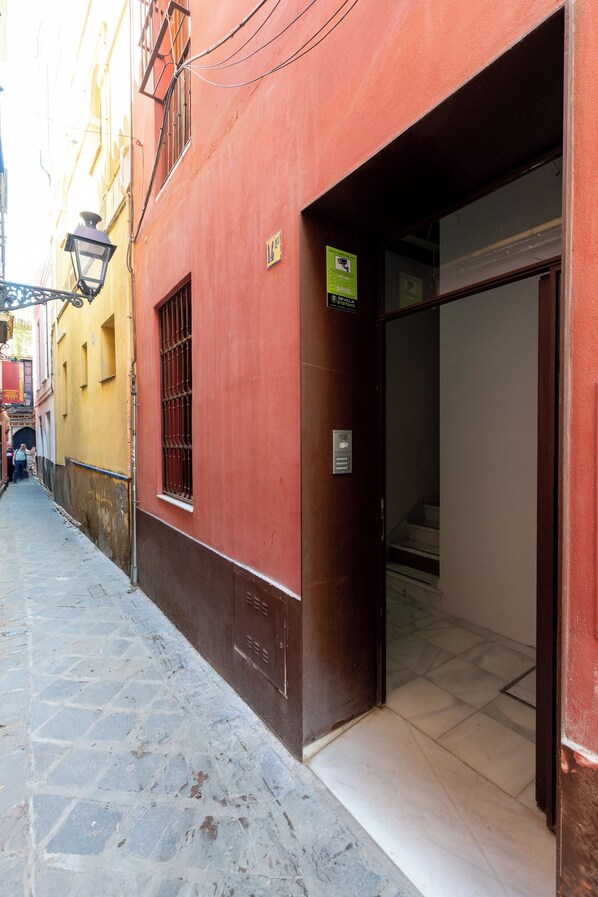 Une rue étroite avec un bâtiment rouge doté d’une grande porte vitrée et d’une petite fenêtre.