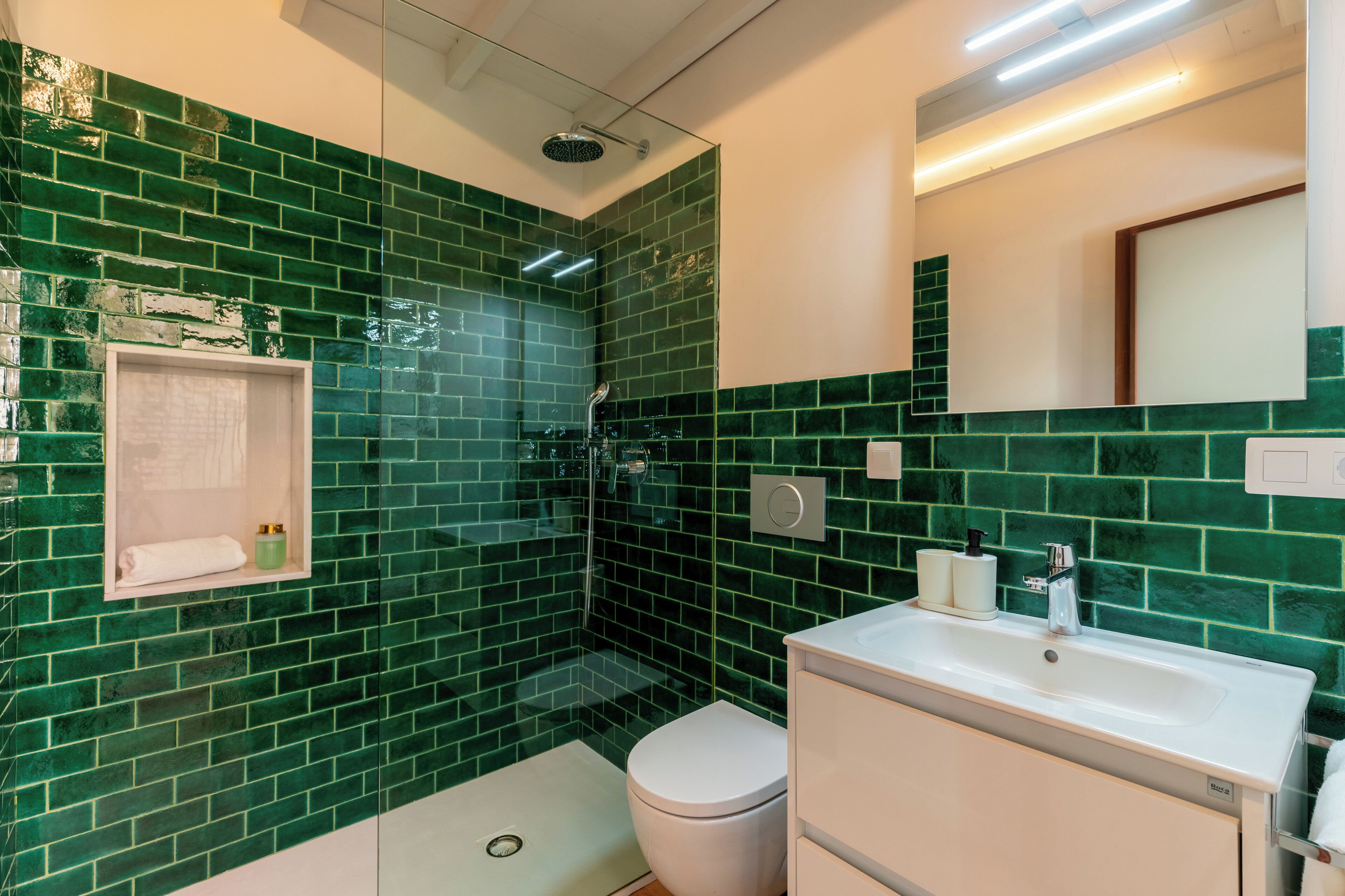A bathroom with green mosaic tiles, a white sink, and a toilet.