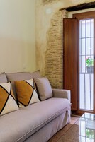 Una sala de estar con un sofá, cojines, una mesa de centro de vidrio, una pared de piedra y una puerta de madera.