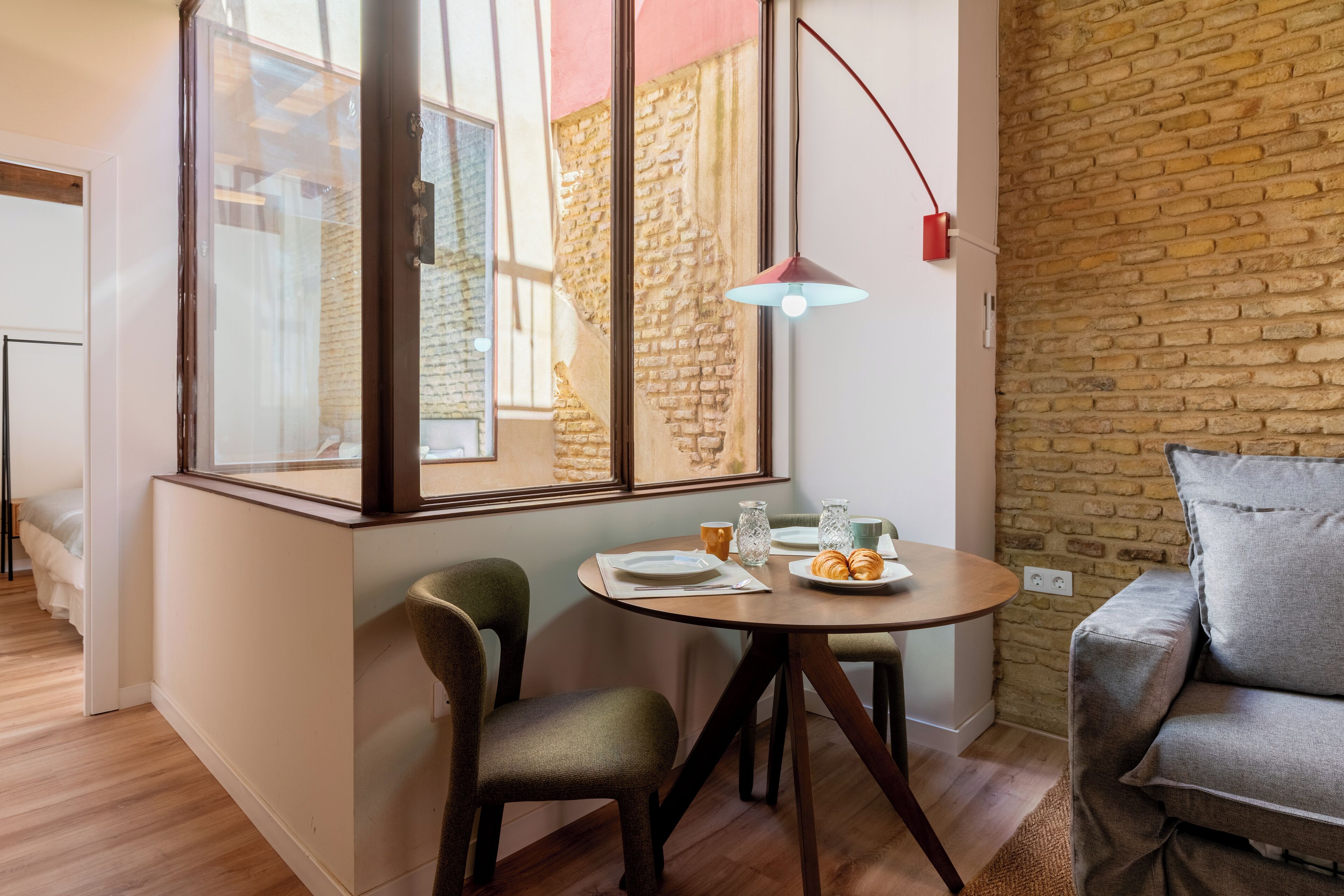 Un coin repas avec une table ronde, deux chaises, une lampe et un mur en briques.