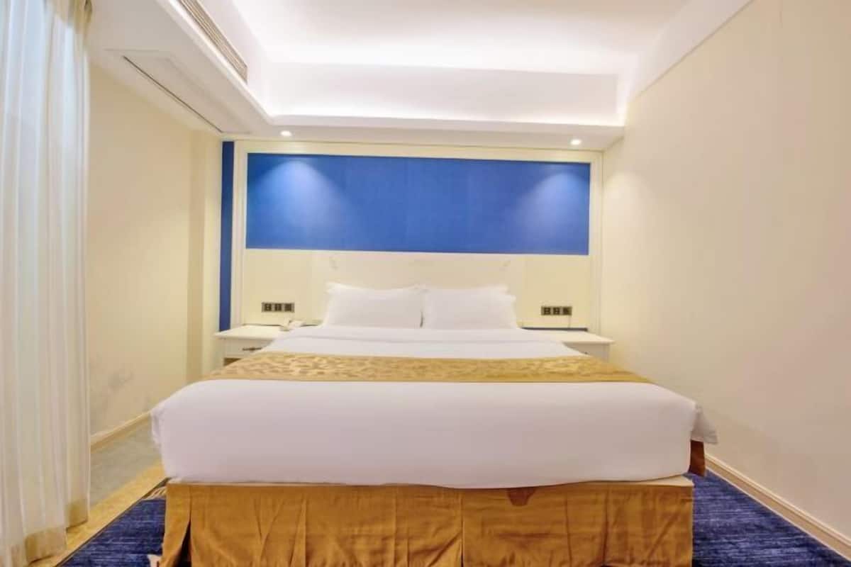 Habitación de hotel con una cama grande, una mesita de noche, un muro decorado en azul y piso alfombrado.