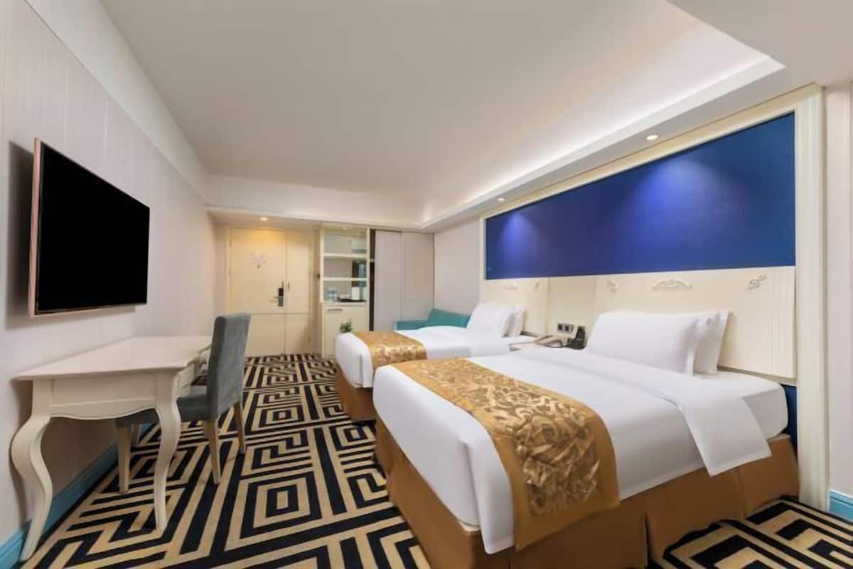 Habitación de hotel con dos camas, un escritorio, una silla, un televisor y una alfombra estampada.