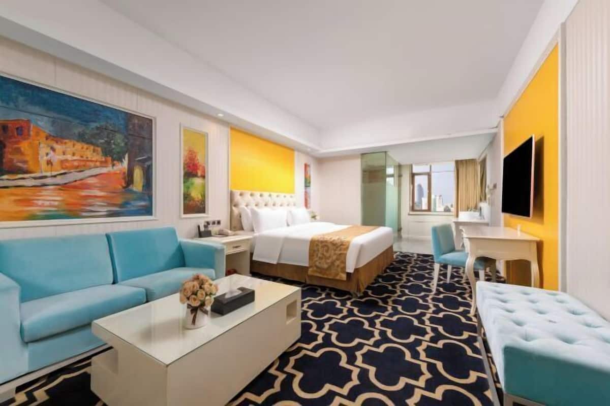 Una habitación de hotel con cama, sofá, escritorio, televisor y un cuadro en la pared.