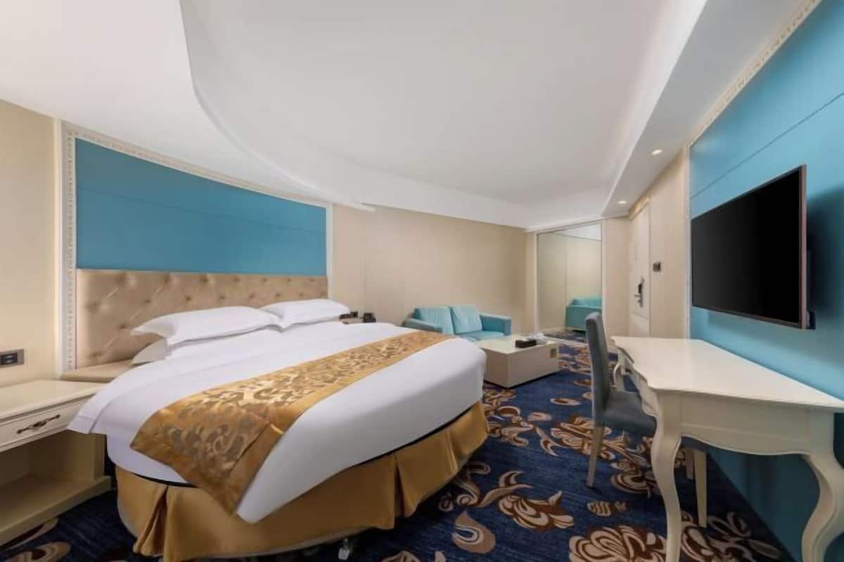 Habitación de hotel con cama, escritorio, televisión y alfombra estampada.