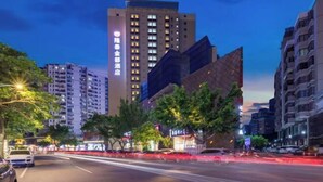 A modern hotel with a prominent sign, surrounded by high-rise buildings and a busy street at dusk. - Longtai Jindu Hotel (Huizhou Ganghui Shopping Center) (Huizhou)
