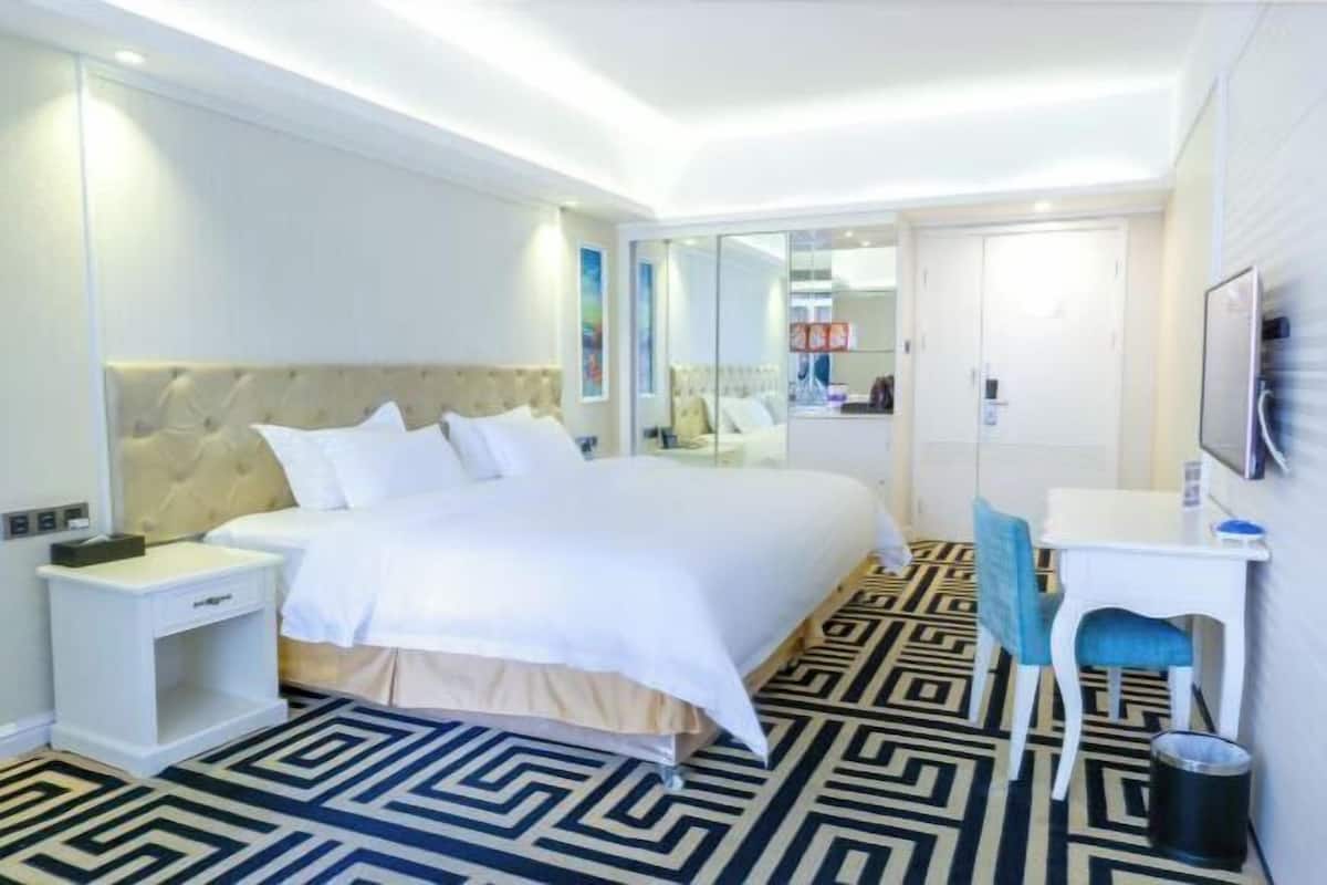 Habitación de hotel con cama, mesita de noche, silla, escritorio y suelo estampado.