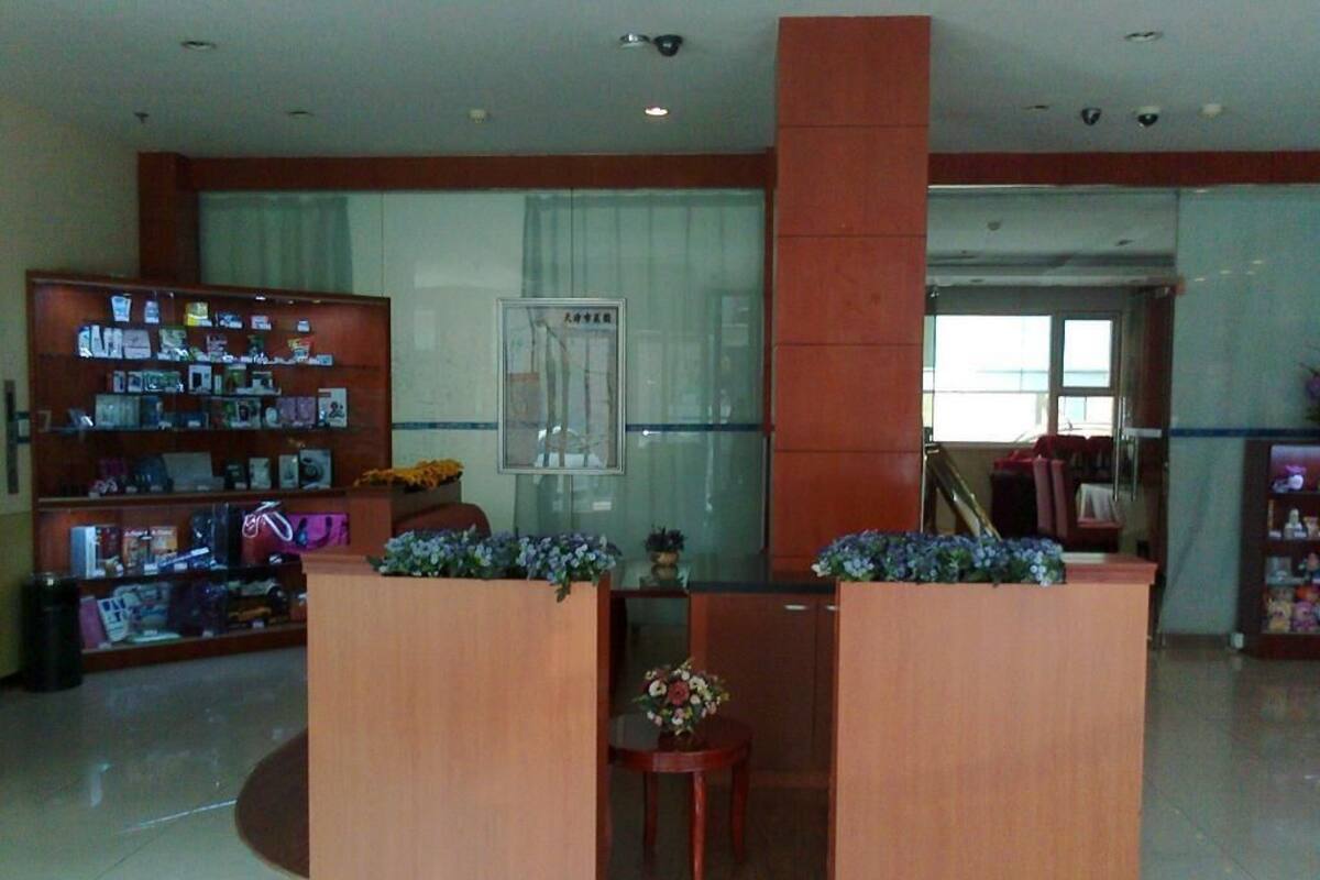 A reception area with a glass partition, a wooden reception desk, a small round table with a floral arrangement, and a bookshelf filled with magazines and brochures.