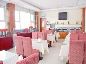 Ein Restaurant mit roten Sitzmöbeln, weißen Tischen und einer Theke mit Fernseher.