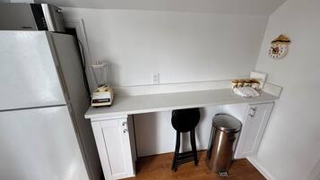 A compact kitchen with a white countertop, a blender, a stainless steel trash can, and a refrigerator.