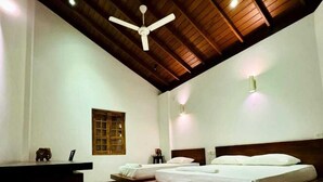 A room with two beds, wooden flooring, a ceiling fan, and a desk with a chair. - Crips Hill Apartments (Galle)