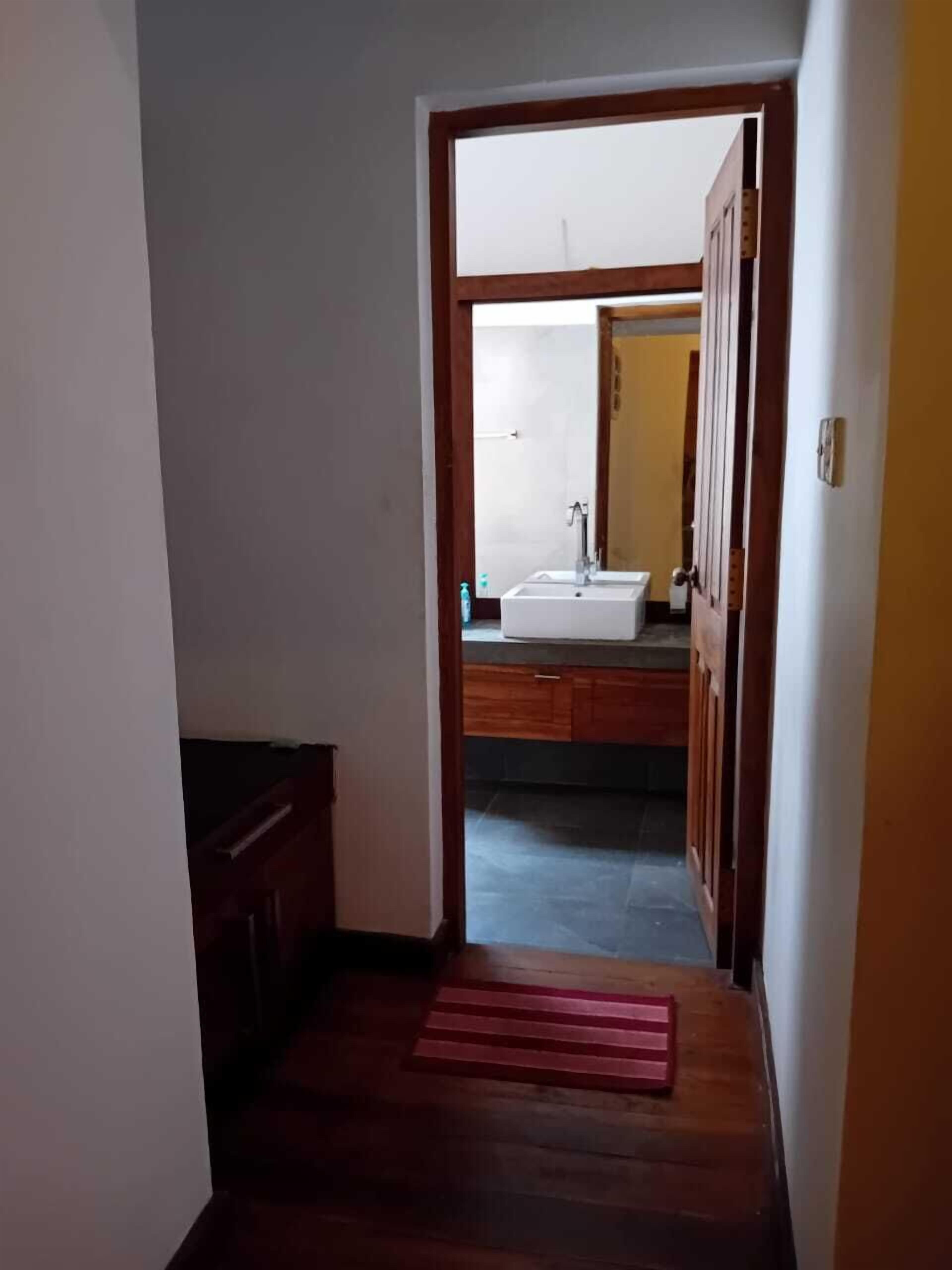 A hallway leading to a bathroom with a sink and mirror.