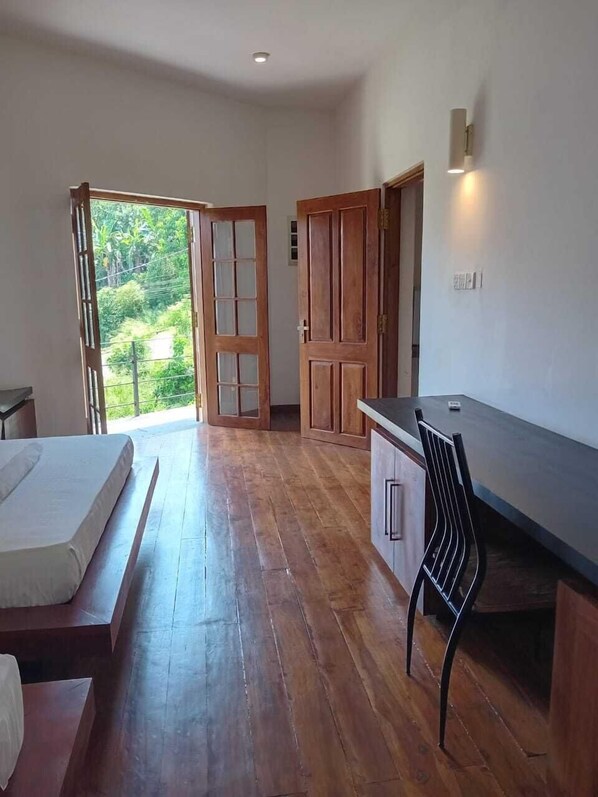 A bedroom with a wooden floor, a bed, a desk, and a chair. - Crips Hill Apartments (Galle)