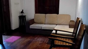 A living room with a sofa, wooden benches, a pink mat, and a dark wooden door. - Crips Hill Apartments (Galle)