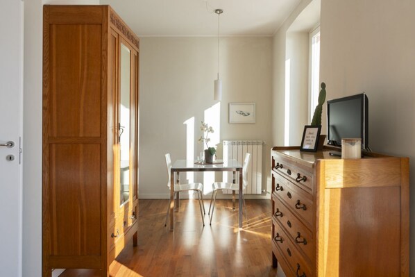 Una habitación con un armario de madera, una mesa de comedor con sillas, un radiador y un televisor sobre un mueble de madera.
