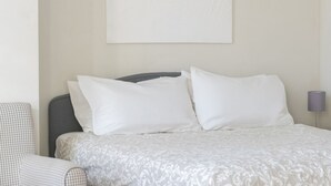 A neatly arranged hotel room with a bed, a chair, and a lamp. - Cadenabbia Lake Side Apartment 3 (Cadenabbia)