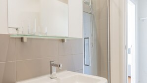 A modern bathroom with a white sink, a glass shelf above it, and a shower area visible through a glass door. - Cadenabbia Lake Side Apartment 3 (Cadenabbia)