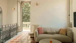 A living room with a sofa, a round coffee table, a patterned rug, a radiator, and a view through an open door.