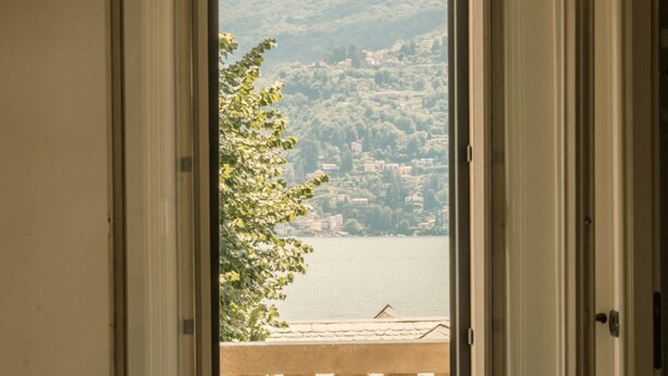 A view from a balcony with a railing, overlooking a lake and a hillside with buildings.