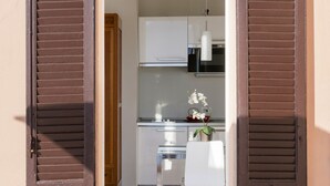 A compact kitchen with white cabinets, a microwave, and a small white chair with a vase of flowers.