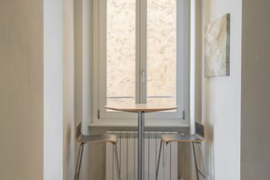 Une pièce d’angle avec une fenêtre, un radiateur et une petite table accompagnée de deux chaises.