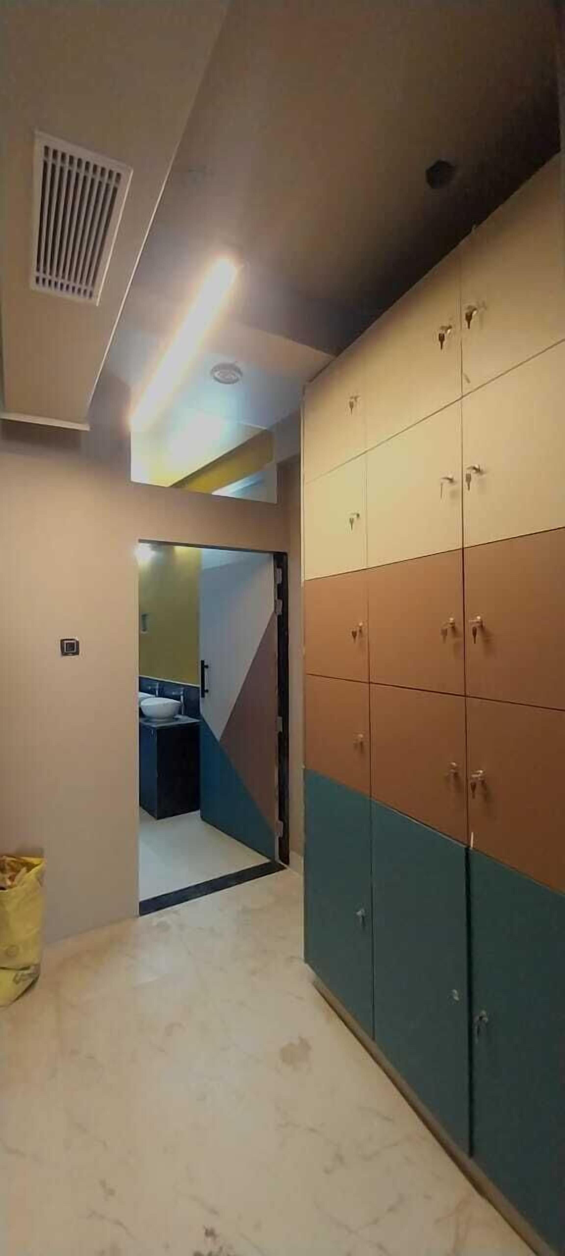 A hallway with lockers, a trash bin, and a glimpse of a bathroom with a sink and toilet.