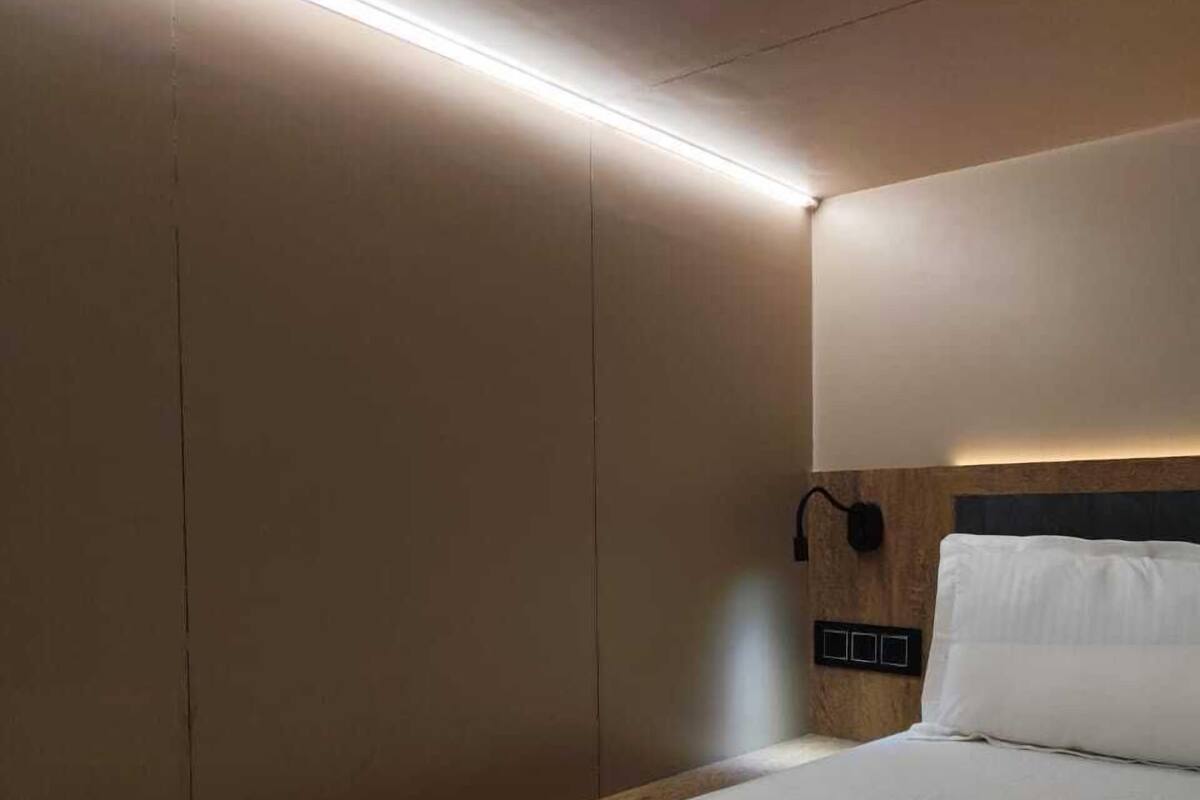 A hotel room with a bed, a wooden headboard, and a wall-mounted control panel.