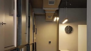 A narrow hallway with a reception desk on the right, featuring a clock and a stone accent wall. - C2 PODS (Varanasi)