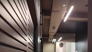 A hallway with a reception desk, a clock, and a modern design with slatted walls and recessed lighting. - C2 PODS (Varanasi)