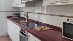 Una cocina moderna con gabinetes blancos, encimera roja y electrodomésticos de acero inoxidable, además de un microondas.