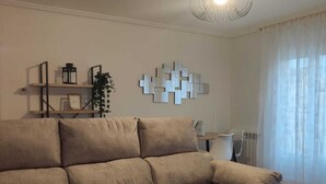 Una sala de estar con un sofá seccional beige grande, una mesita de madera, un adorno en la pared y una lámpara de techo.