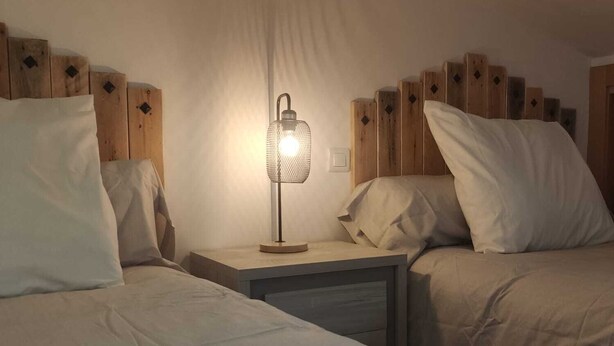 Habitación de hotel con dos camas, una mesita de noche y una lámpara fijada a la pared.