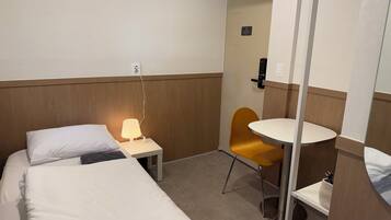 A hotel room with a bed, a bedside lamp, a small table, a chair, and a mirror.