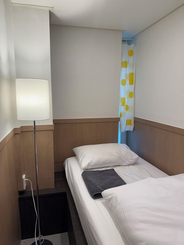 A hotel room with a bed, a bedside lamp, a curtain, and a wall-mounted outlet.