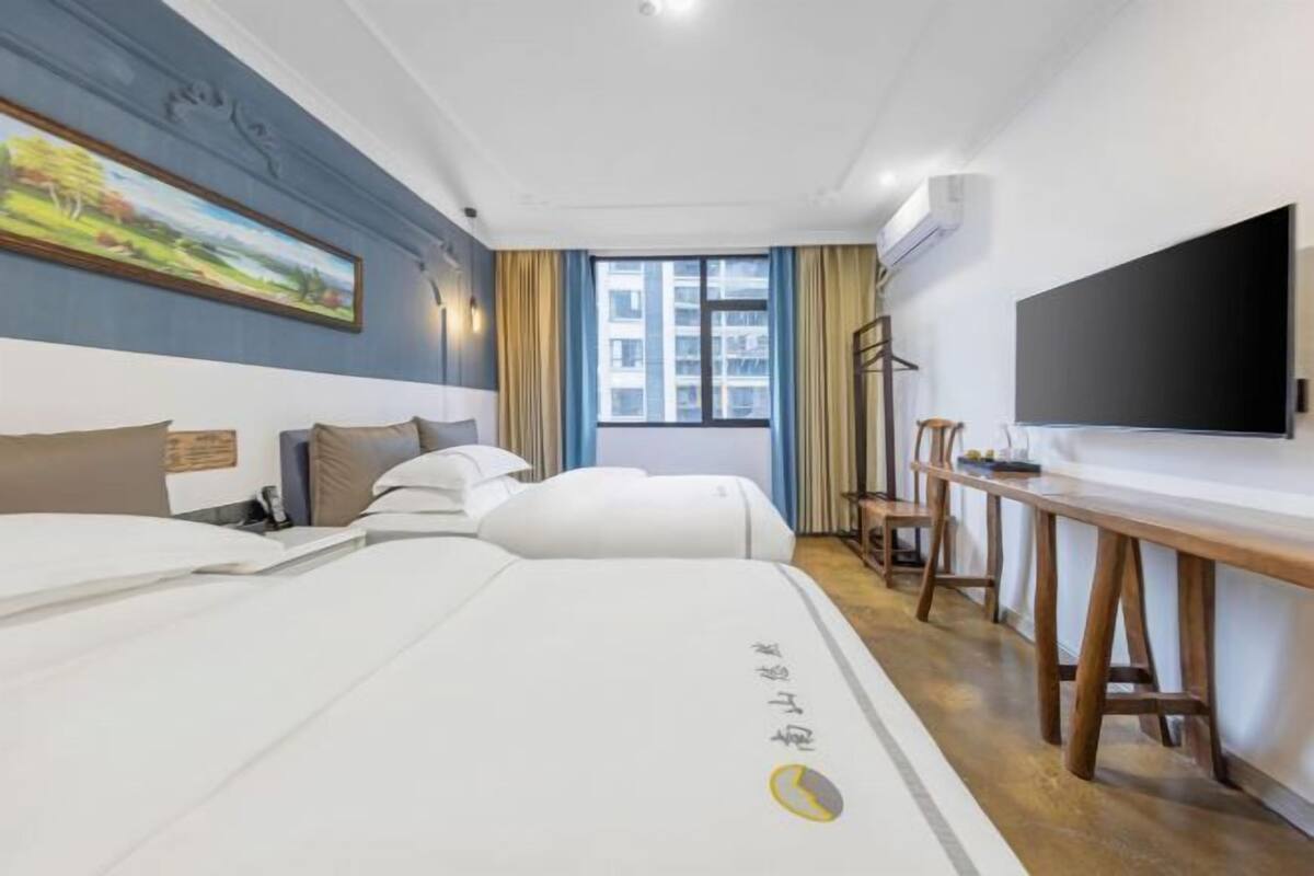 Quarto de hotel com cama, escrivaninha, cadeira, televisão e janela com cortinas.