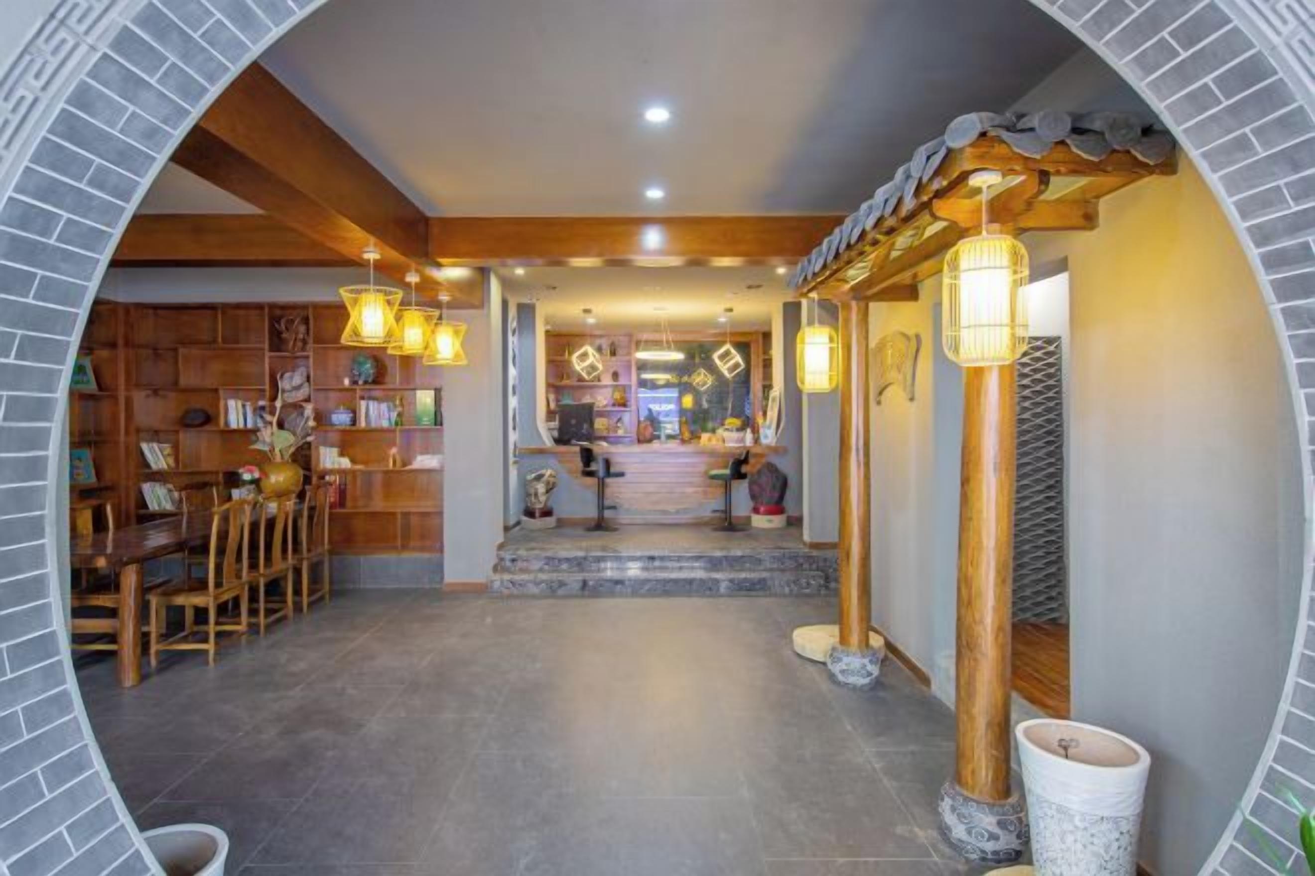 A hallway with a wooden staircase leading to a reception area, a seating area with chairs, and a bookshelf.