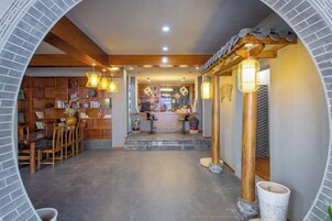 A hallway with a wooden staircase leading to a reception area, a seating area with chairs, and a bookshelf.