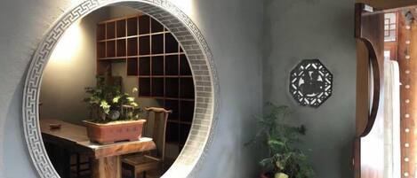 A room with a round mirror, a wooden dining table, and chairs. There is a potted plant on the floor.