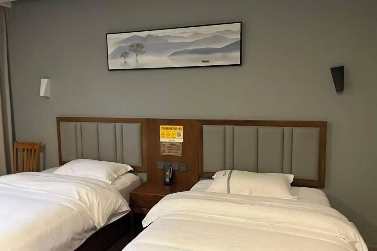 Quarto de hotel com duas camas, uma cabeceira de madeira, um quadro de uma paisagem e uma placa na cabeceira.