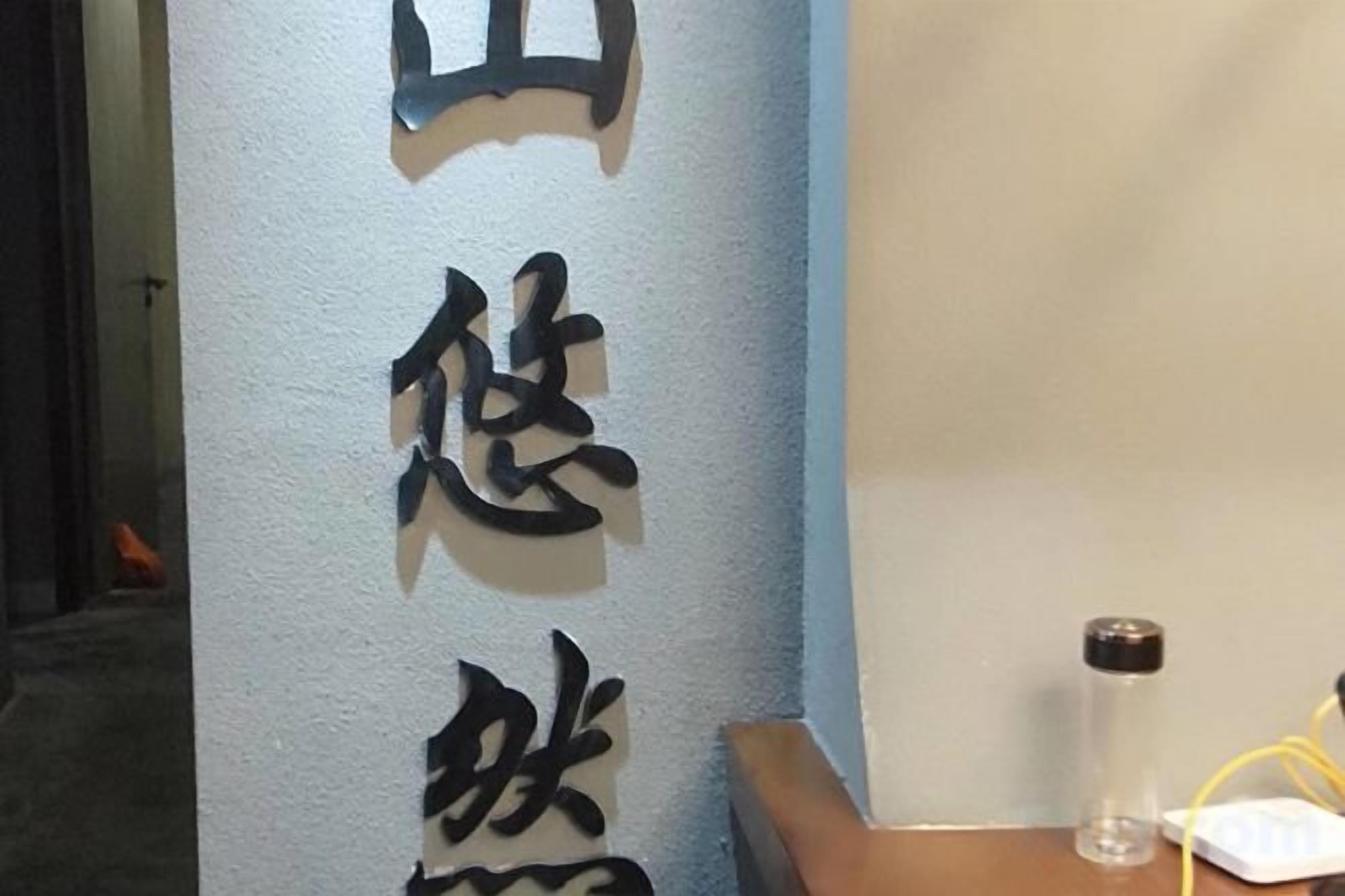 A vertical sign with Chinese characters, a clear glass bottle, and a white object on a wooden surface.