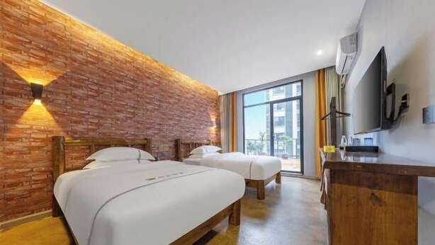 Ein Hotelzimmer mit zwei Betten, einem Holztisch, einem Fernseher und einer Ziegelwand.