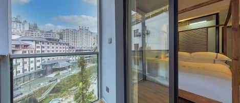 A balcony with a city view, a bed with a wooden headboard, and a glass door leading to a room.