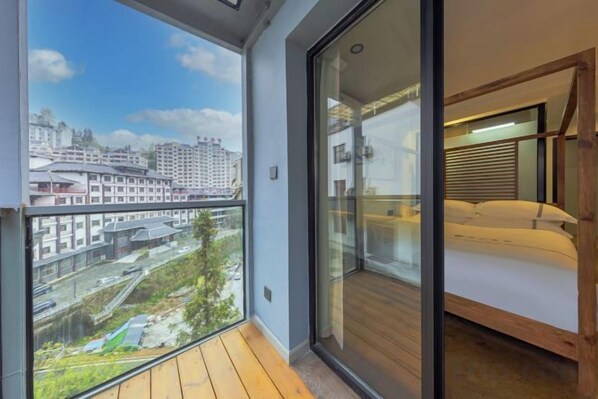 A balcony with a city view, a bed with a wooden headboard, and a glass door leading to a room.