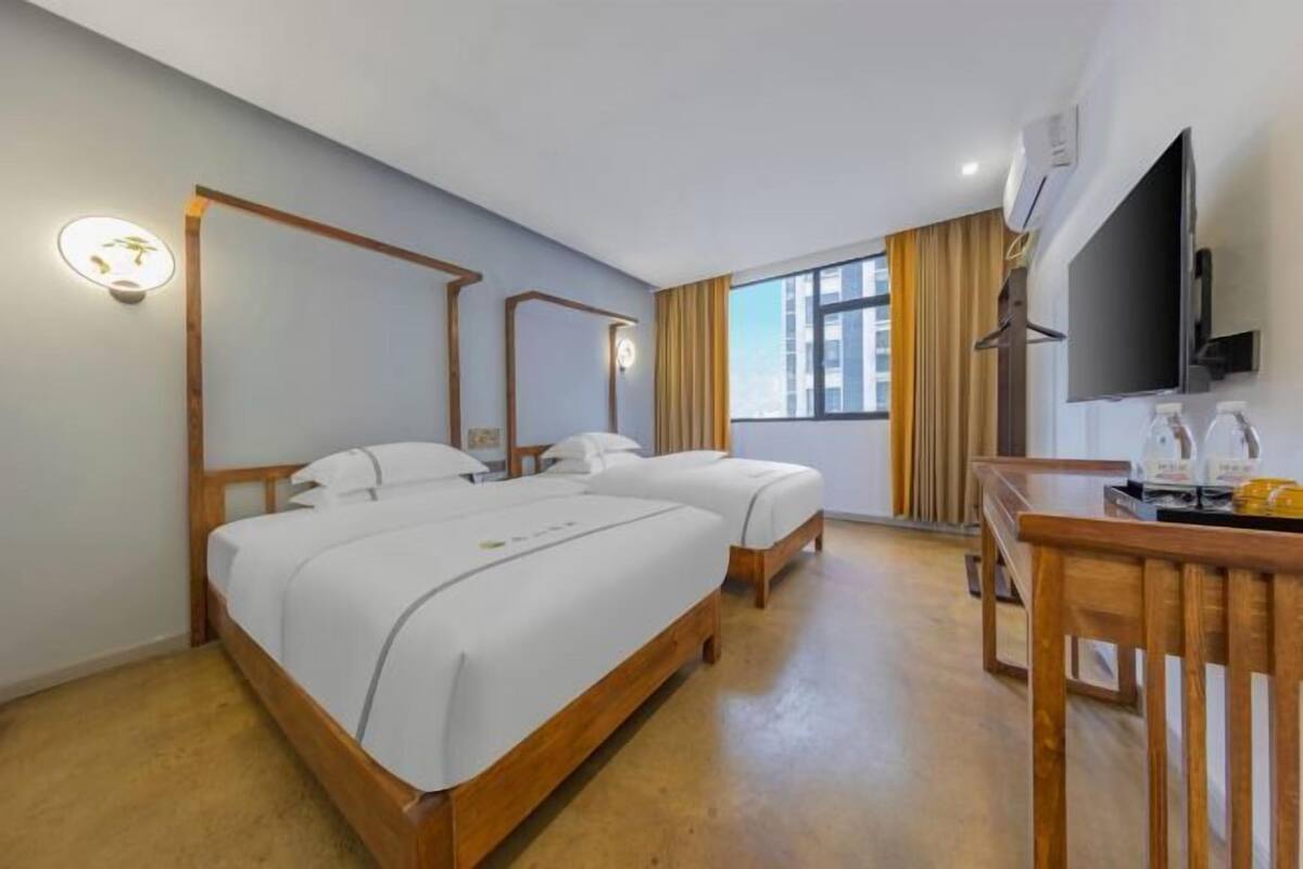 Quarto de hotel com duas camas, uma secretária de madeira, televisão de tela plana e janela com cortinas.