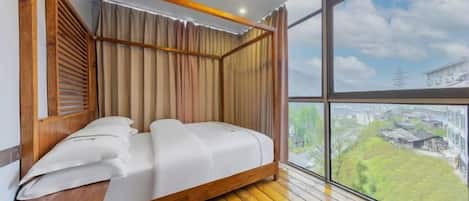 Un dormitorio con estructura de cama de madera, vista panorámica de la ciudad a través de amplias ventanas y techo inclinado.