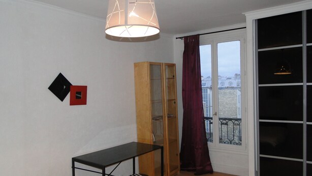A room with a black table, a red chair, a wooden cabinet, and a large window with curtains. - Apartment Trocadero (Paris)